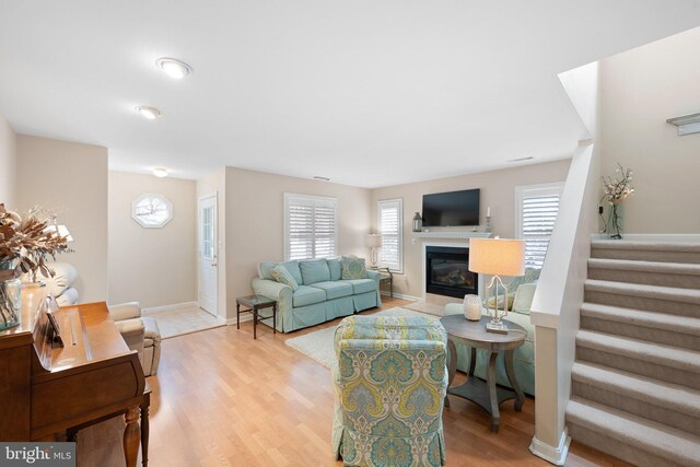 living area featuring a glass covered fireplace, stairway, light wood-style floors, and a wealth of natural light