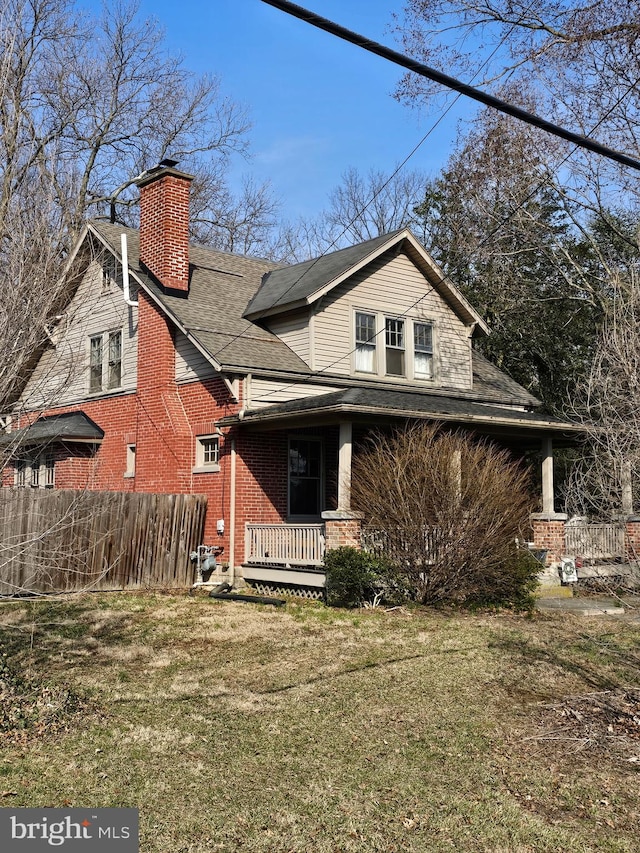 view of front facade featuring brick siding, fence, a front yard, covered porch, and a chimney