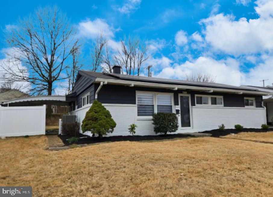 ranch-style house featuring central AC unit, a chimney, solar panels, and a front lawn