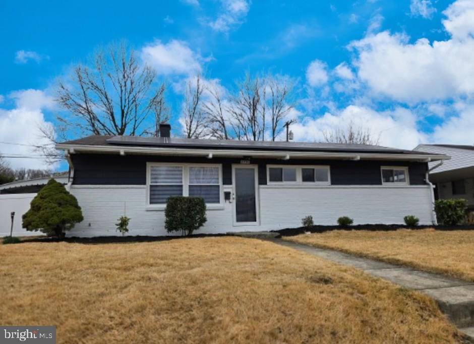 single story home featuring roof mounted solar panels and a front lawn