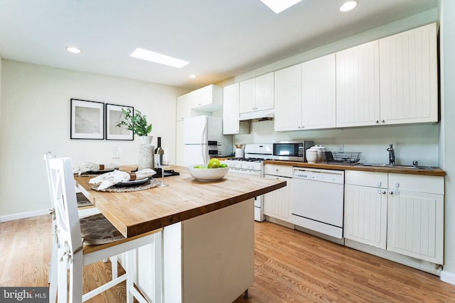 kitchen featuring wooden counters, under cabinet range hood, light wood-style flooring, white appliances, and a sink