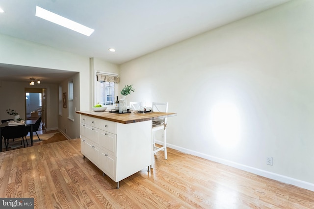 kitchen with wooden counters, baseboards, a breakfast bar area, light wood-style floors, and white cabinetry