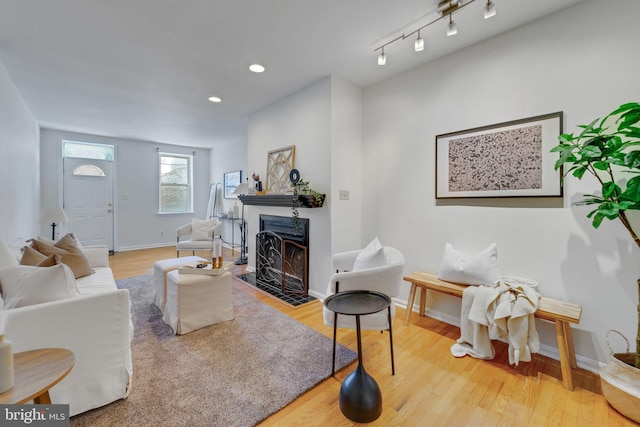 living room featuring recessed lighting, a fireplace with flush hearth, wood finished floors, and baseboards