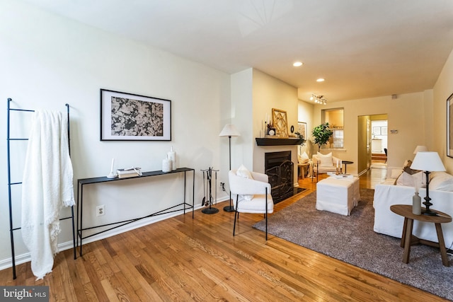 living area featuring a fireplace with flush hearth, wood finished floors, recessed lighting, and baseboards