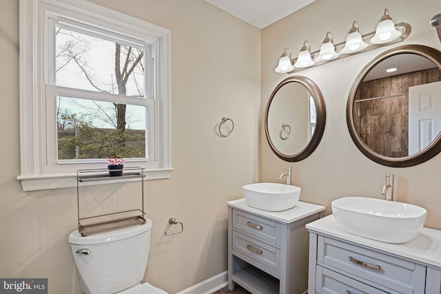 bathroom with a sink, baseboards, toilet, and two vanities