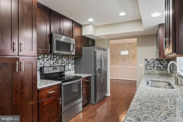 kitchen with dark brown cabinets, light stone countertops, dark wood-style floors, stainless steel appliances, and a sink