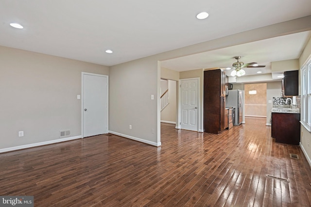 unfurnished living room featuring dark wood finished floors, baseboards, visible vents, and a ceiling fan