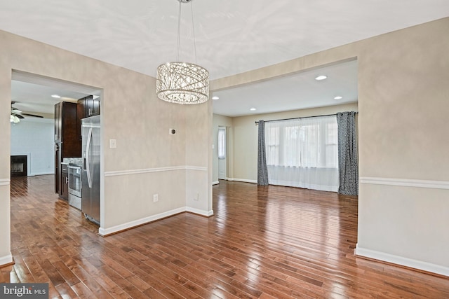 unfurnished room with baseboards, a fireplace, recessed lighting, wood-type flooring, and ceiling fan with notable chandelier