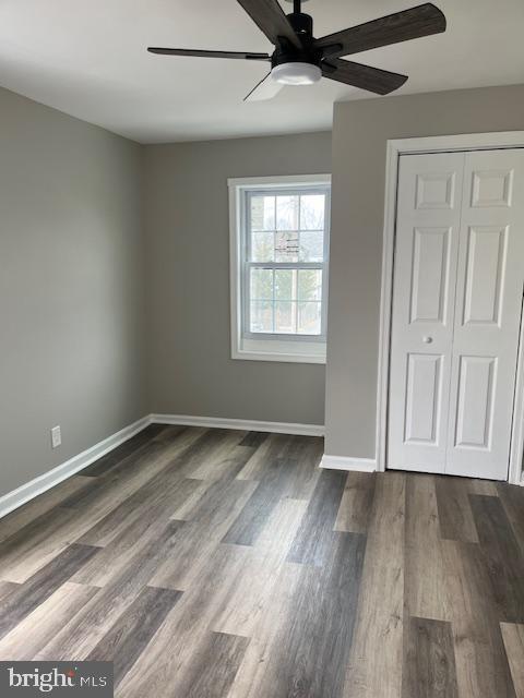 unfurnished bedroom featuring a ceiling fan, baseboards, dark wood-style flooring, and a closet