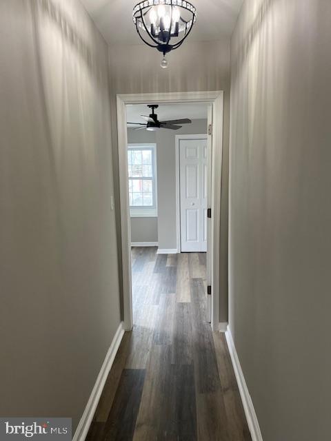 hallway featuring dark wood finished floors, a notable chandelier, and baseboards