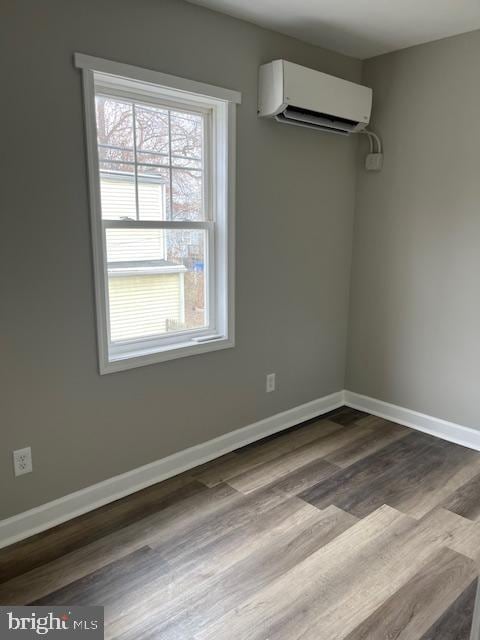 empty room with baseboards, dark wood finished floors, and a wall mounted AC