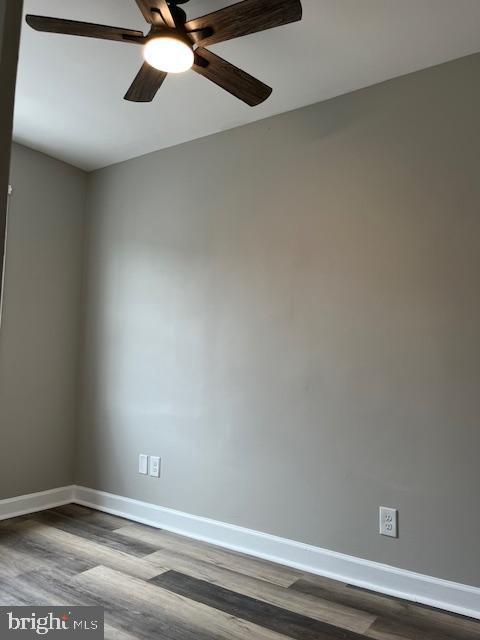 spare room featuring baseboards, dark wood-style floors, and a ceiling fan