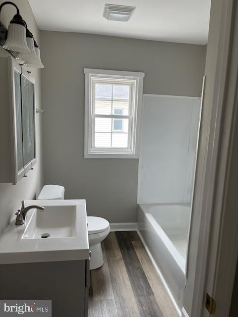 bathroom featuring visible vents, toilet, a washtub, wood finished floors, and vanity