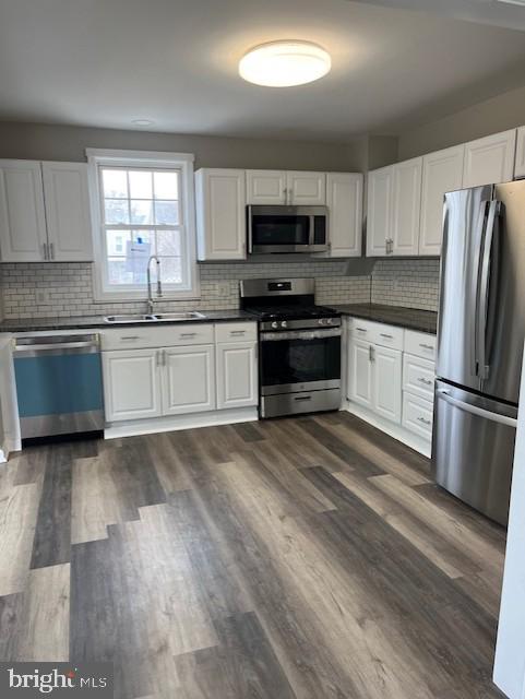 kitchen featuring a sink, dark countertops, appliances with stainless steel finishes, and white cabinetry