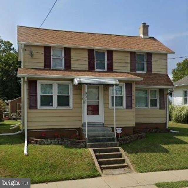 traditional-style house featuring a front yard, entry steps, and a chimney
