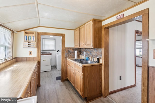 kitchen featuring washer and dryer, a sink, light countertops, light wood-style floors, and vaulted ceiling