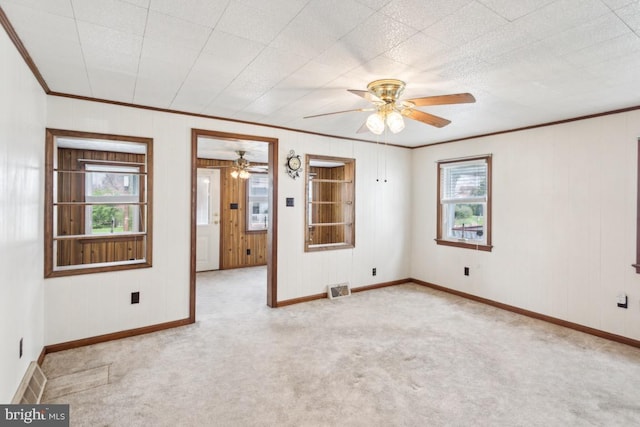 spare room with baseboards, ornamental molding, visible vents, ceiling fan, and light colored carpet