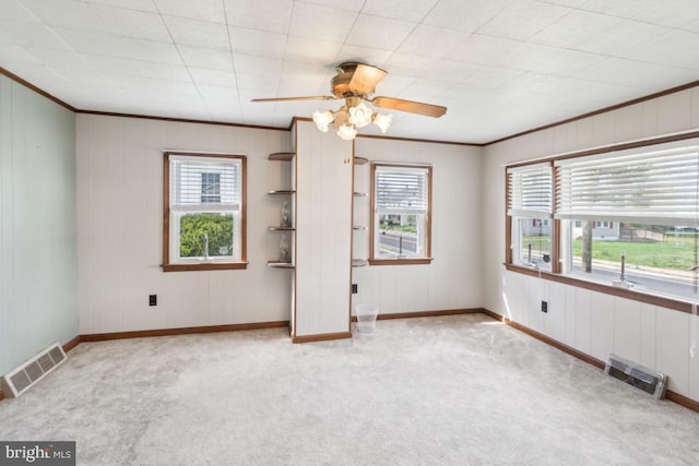carpeted empty room featuring ornamental molding, visible vents, ceiling fan, and plenty of natural light