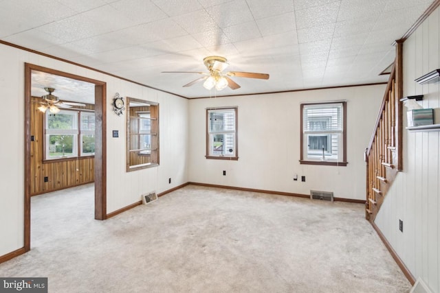 empty room with ceiling fan, light colored carpet, ornamental molding, visible vents, and stairs