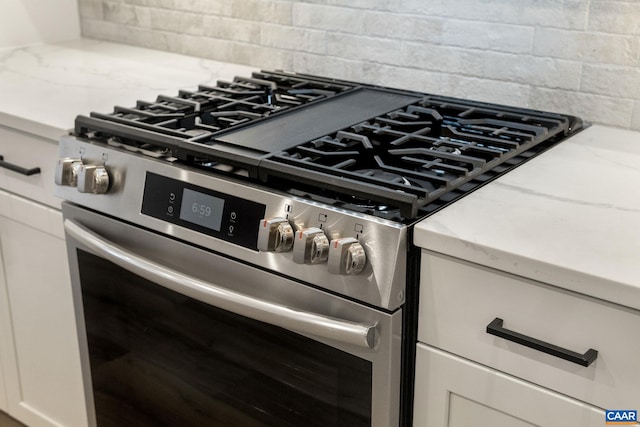 interior details featuring decorative backsplash, white cabinets, light stone counters, and gas stove