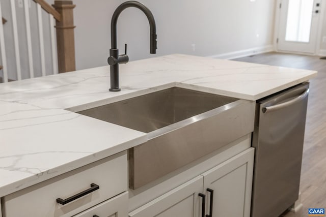 details with light stone counters, white cabinetry, a sink, light wood-style floors, and stainless steel dishwasher