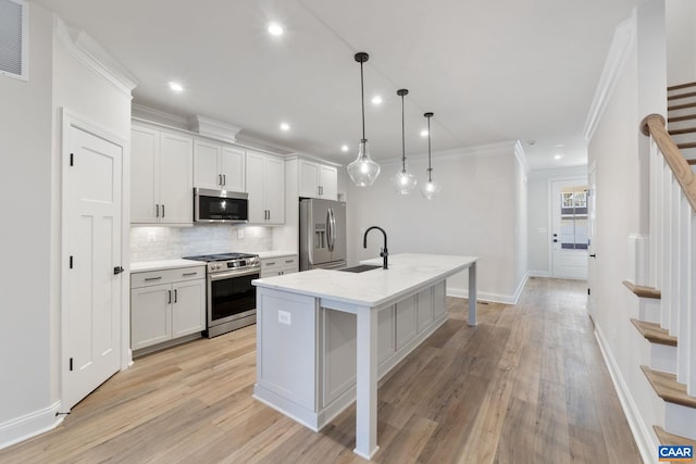 kitchen featuring an island with sink, a sink, backsplash, appliances with stainless steel finishes, and crown molding