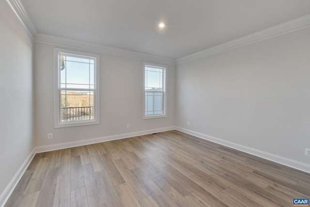 empty room featuring plenty of natural light, wood finished floors, baseboards, and ornamental molding