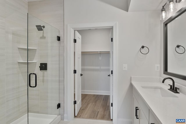 full bath with a spacious closet, a shower stall, vanity, and baseboards