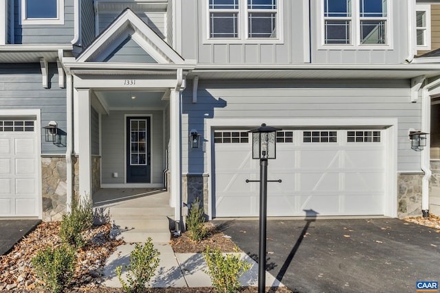 property entrance featuring stone siding, driveway, board and batten siding, and an attached garage