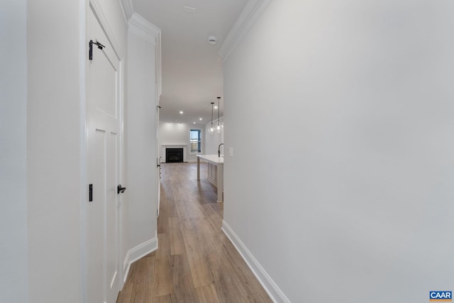 hallway featuring crown molding, baseboards, and light wood-type flooring