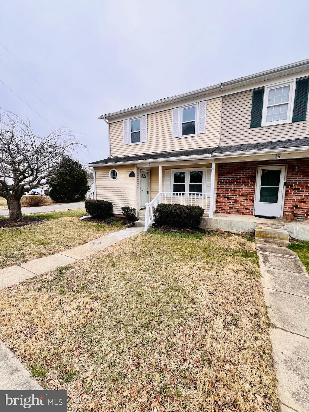 multi unit property featuring brick siding, a porch, and a front lawn