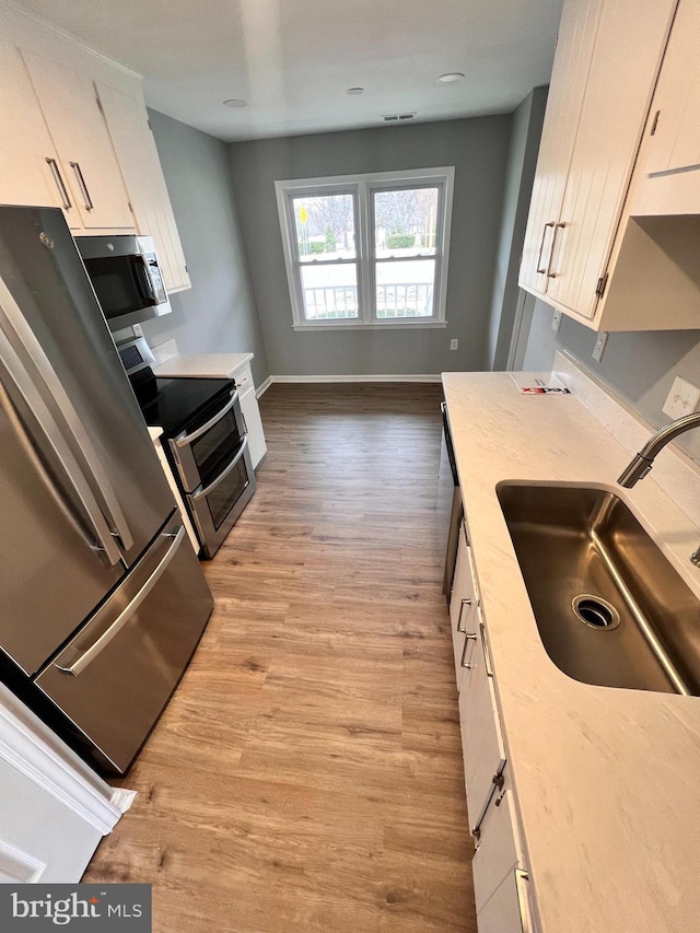 kitchen featuring light wood finished floors, a sink, stainless steel appliances, light countertops, and white cabinetry