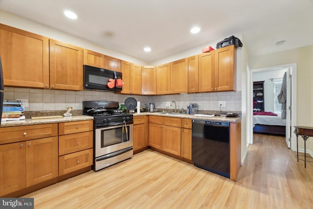 kitchen featuring a sink, decorative backsplash, black appliances, and light wood finished floors