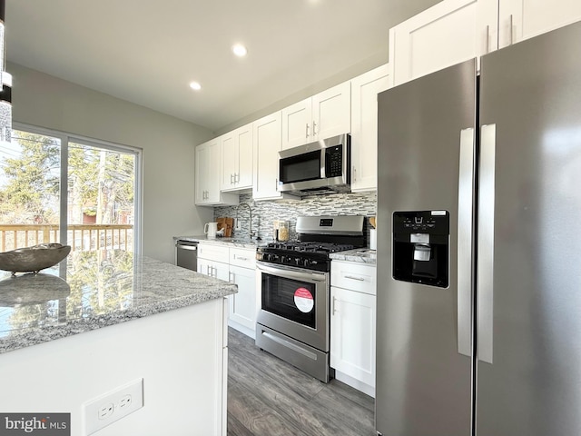 kitchen featuring light stone counters, wood finished floors, appliances with stainless steel finishes, white cabinetry, and backsplash