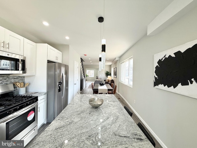 kitchen featuring dark wood-type flooring, decorative light fixtures, light stone counters, appliances with stainless steel finishes, and white cabinetry