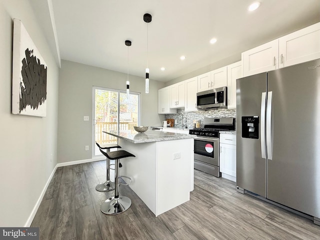 kitchen with a kitchen island, wood finished floors, stainless steel appliances, white cabinets, and decorative backsplash