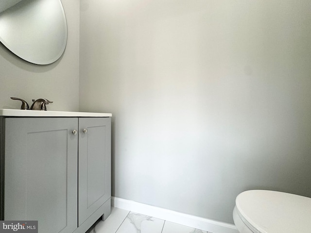 half bathroom featuring marble finish floor, toilet, vanity, and baseboards