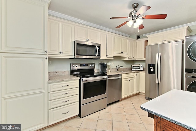 kitchen featuring cream cabinetry, appliances with stainless steel finishes, and stacked washer / dryer