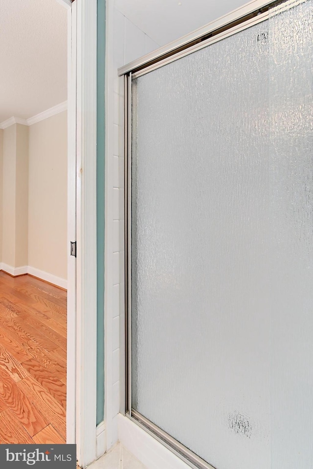 full bathroom with a stall shower, baseboards, wood finished floors, and crown molding