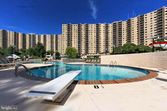 community pool with a patio area, a view of city, and a diving board