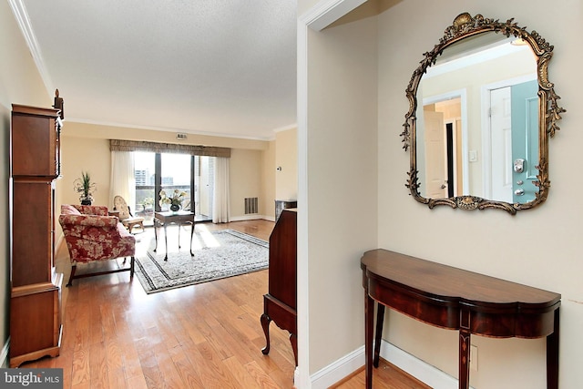 hall featuring visible vents, baseboards, wood finished floors, and ornamental molding