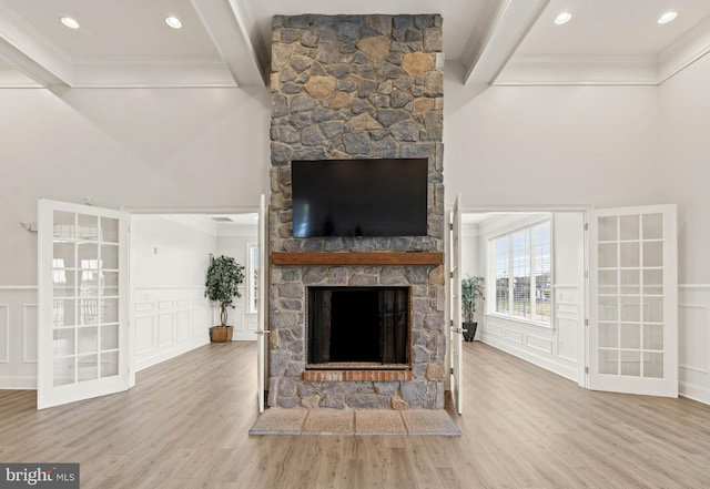 unfurnished living room featuring beam ceiling, a stone fireplace, a decorative wall, and wood finished floors