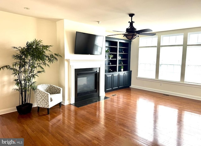 unfurnished living room with wood finished floors, a ceiling fan, baseboards, visible vents, and a fireplace with flush hearth