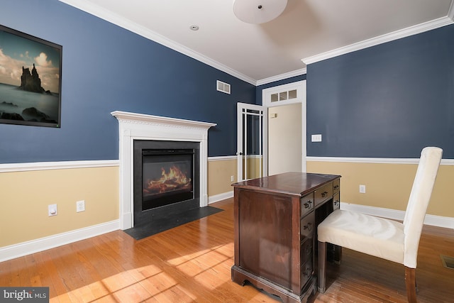 office space featuring wood finished floors, visible vents, baseboards, a fireplace with flush hearth, and crown molding