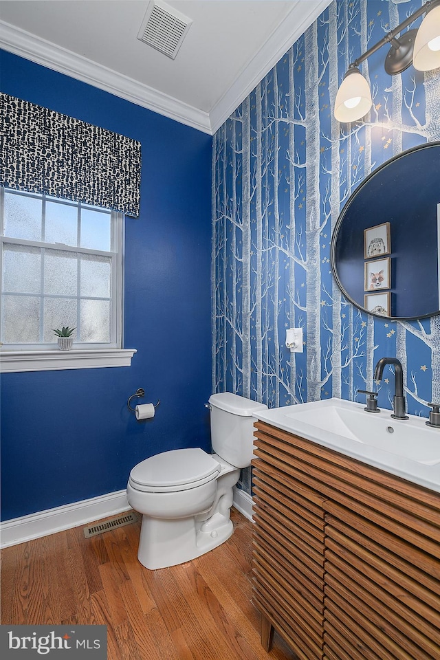 half bathroom with visible vents, toilet, wood finished floors, and ornamental molding