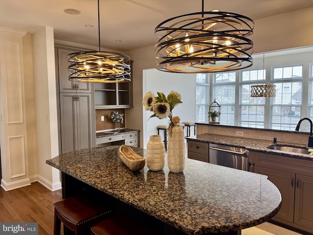 kitchen with dark wood-type flooring, a kitchen bar, stainless steel dishwasher, a notable chandelier, and a sink