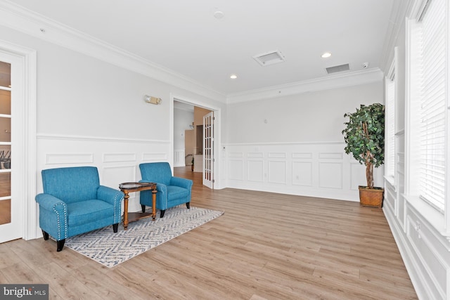 living area featuring wainscoting, visible vents, light wood-style flooring, and crown molding