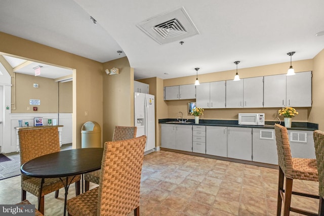 kitchen with white appliances, visible vents, a sink, hanging light fixtures, and dark countertops