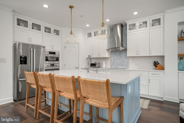 kitchen with backsplash, a center island with sink, light countertops, appliances with stainless steel finishes, and wall chimney exhaust hood