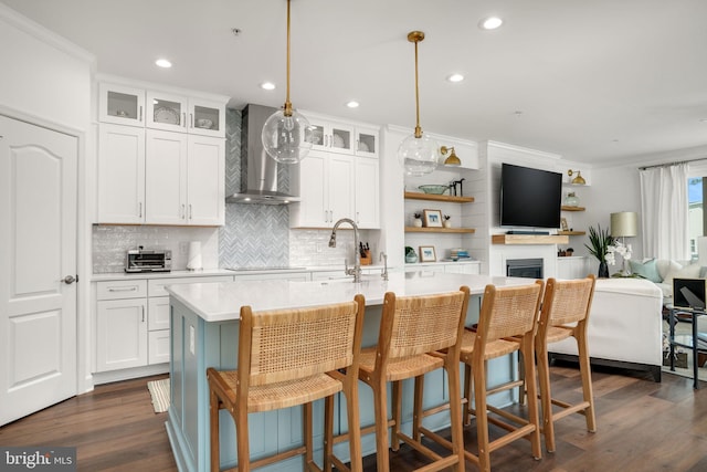 kitchen featuring a kitchen island with sink, a sink, dark wood-type flooring, light countertops, and wall chimney range hood